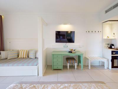 Bright hotel room with bed, desk, chair, and modern kitchen area.