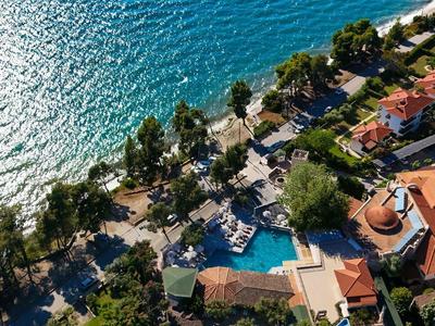 Aerial view of a resort with pool, tennis court, and sparkling sea view.