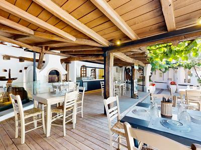 Offener, hell beleuchteter Hotelrestaurantbereich mit Holzboden, weißen Stühlen und grünem Blätterdach.