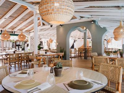 Helles Restaurant mit Holzdach, runden Tischen und geflochtenen Stühlen im Urlaubsort.