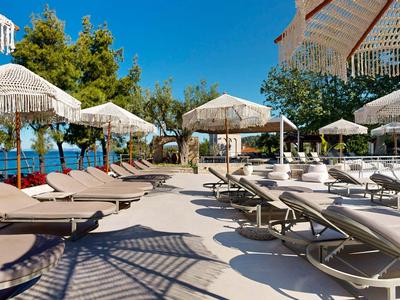 Sonnige Terrasse mit Liegestühlen und Schirmen an einem Hotelpool.