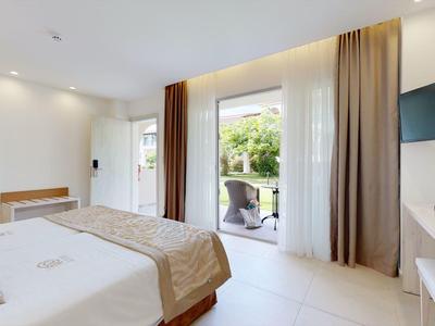 Bright hotel room with double bed, TV, desk, and access to a balcony overlooking the garden.