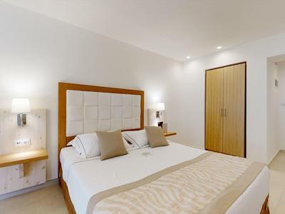 Bright hotel room with large bed, nightstands, and closet in warm tones.