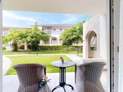 View from a room onto a terrace with two chairs and a small table overlooking a green garden.