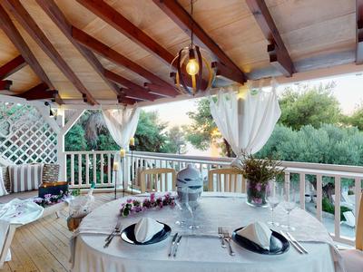 Ampia terrazza in legno con tavolo apparecchiato e comoda zona salotto sotto tetto in legno.