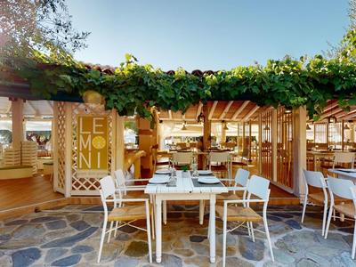 Outdoor restaurant with tables and chairs under a green wooden pergola on a clear sky day.