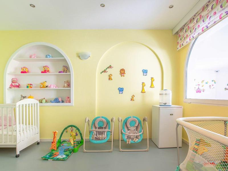 Bright yellow nursery with crib, toys, and two small chairs next to a high chair.