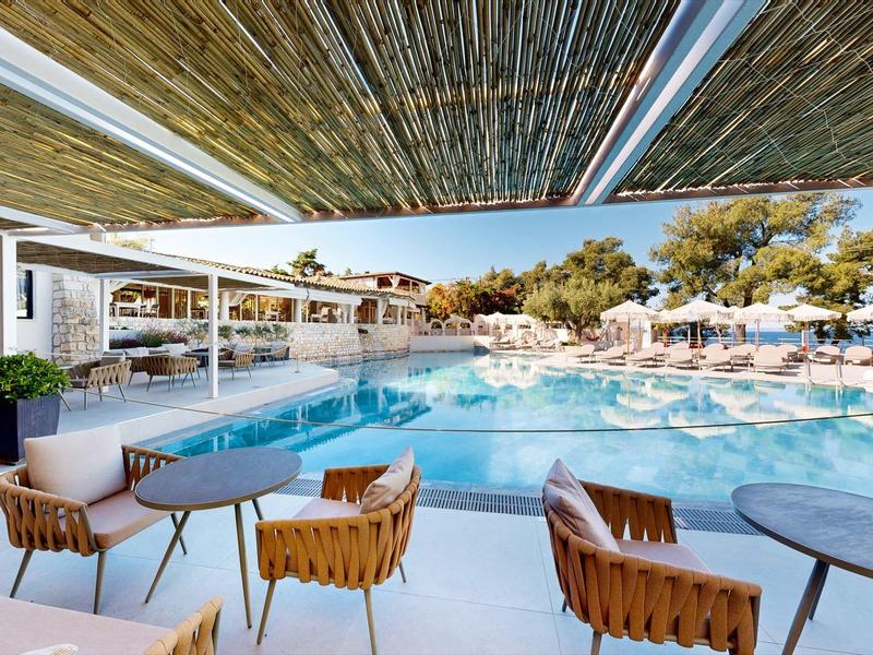 Modern pool area with sun umbrellas and seating under a wooden pergola.