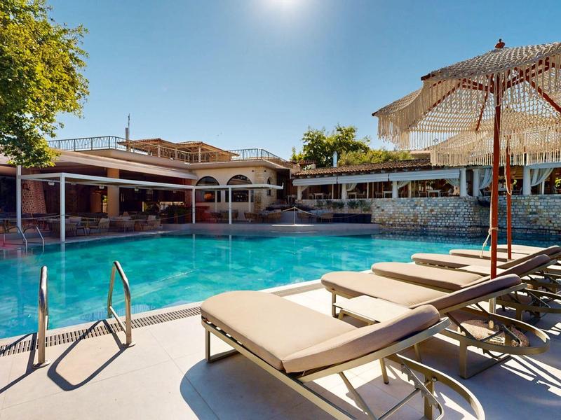 Hotel pool with sun loungers and umbrella in sunny weather
