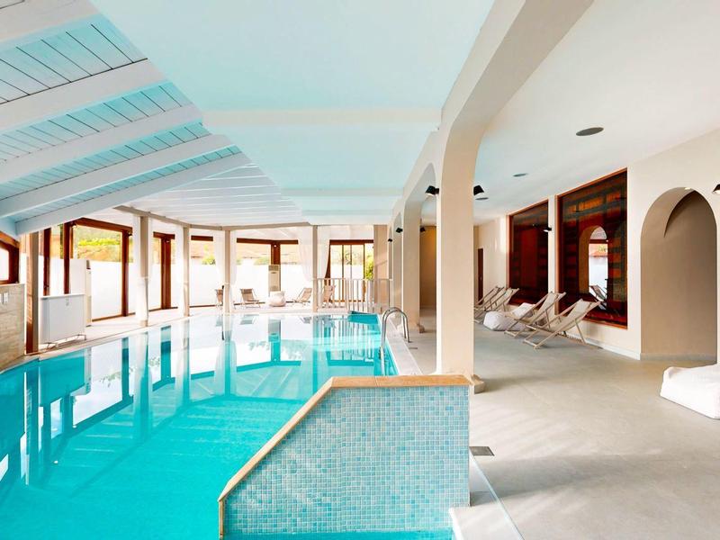 Indoor area with large heated pool, lounge chairs, and modern amenities in a hotel.