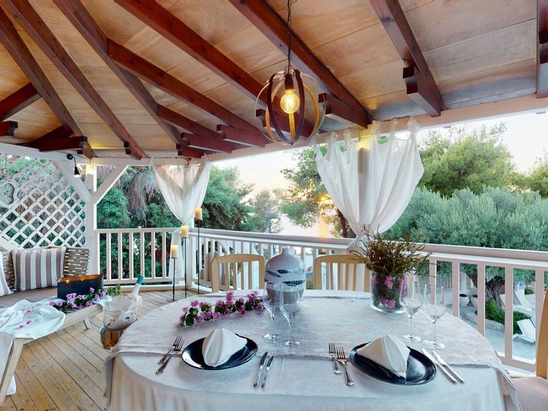 Rustic terrace with wooden beams, set dining table, and view of green trees.