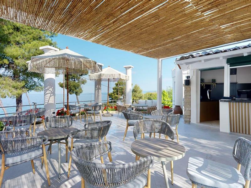Sunny terrace with shade, glass chairs, and sea view at a hotel restaurant