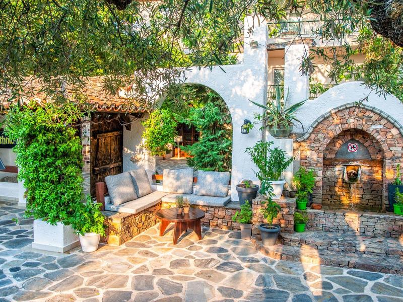 Cozy patio with garden sofa, fireplace, and white house wall under trees.