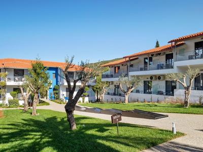 Hotel complex with two-story buildings, garden with grass, trees, and a barbecue under a blue sky.