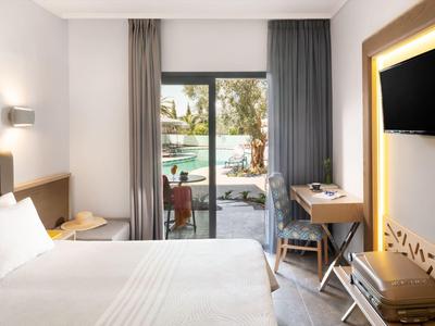 Chambre d'hôtel lumineuse avec lit, bureau, télévision et porte coulissante vers piscine extérieure.