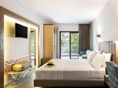 Chambre d'hôtel moderne avec grand lit, TV, balcon et lumière naturelle.