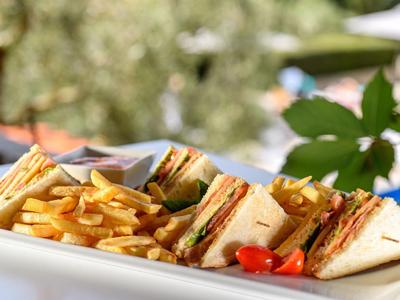 Assiette avec sandwiches, frites et tomates cerises sur un plateau blanc en extérieur.