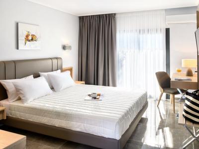 Jasny pokój hotelowy z dużym łóżkiem, biurkiem i dostępem do balkonu.