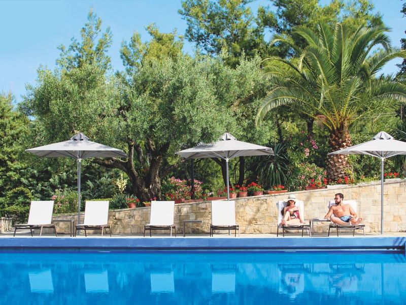 Chaises longues au bord de la piscine avec parasols et palmiers dans un jardin d'hôtel ensoleillé.