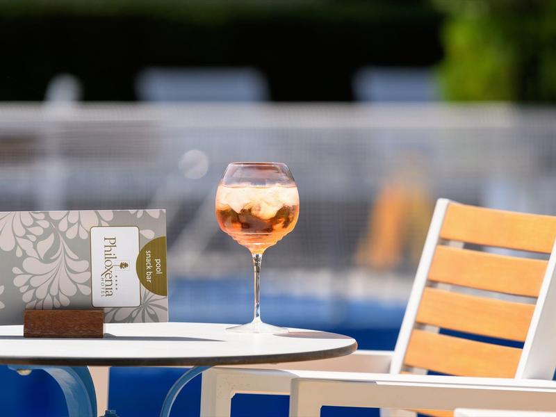 Un verre de vin rosé sur une table blanche à côté d'une chaise en bois près de la piscine.