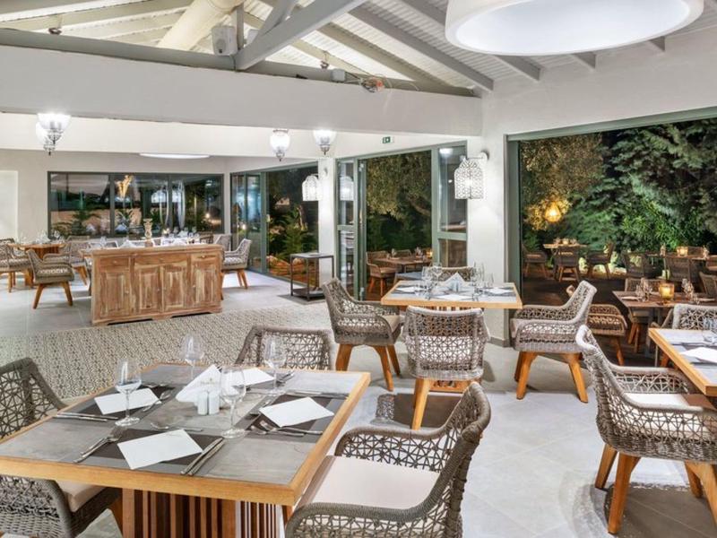 Grand espace de restaurant extérieur avec tables en bois, chaises et mur végétal la nuit.