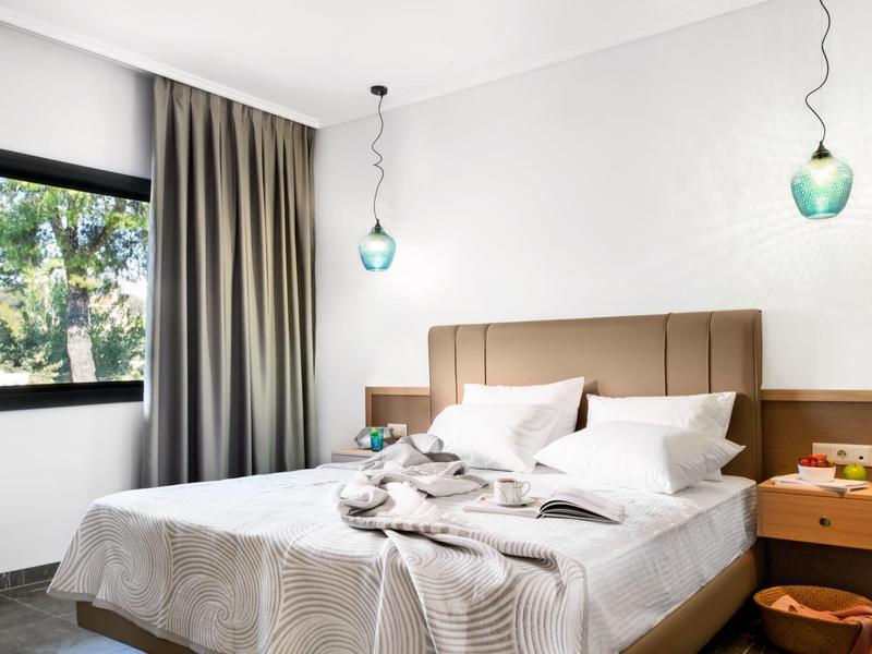 Chambre moderne avec grand lit, tête de lit beige, fenêtre et tables de chevet avec lampes.