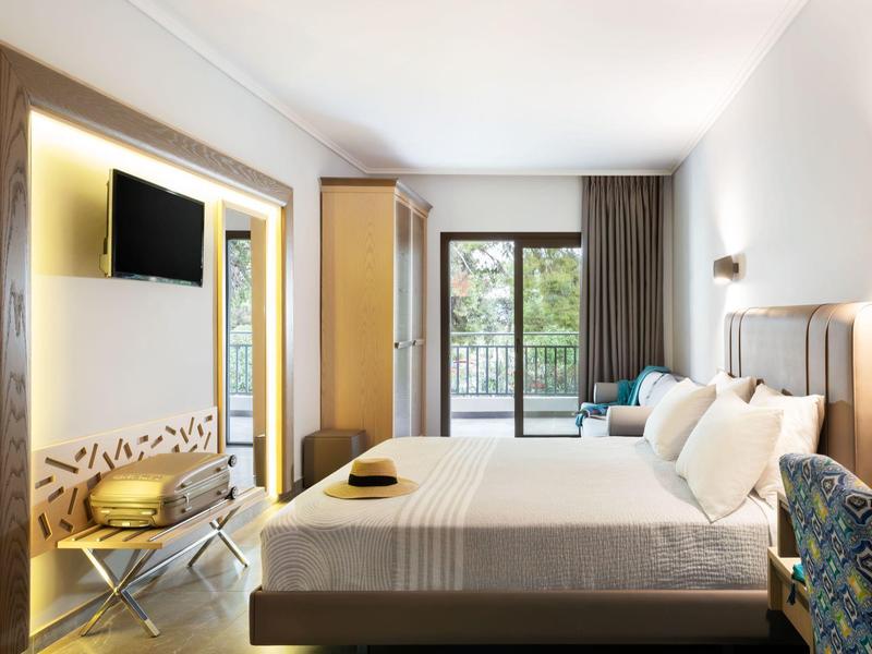 Chambre d'hôtel moderne avec grand lit, TV, balcon et lumière naturelle.