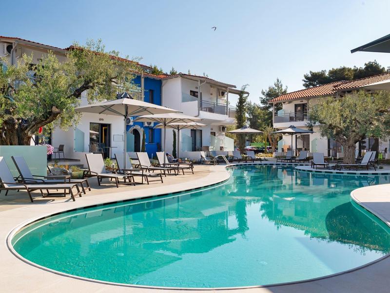 Piscine extérieure entourée de chaises longues et de bâtiments blancs à deux étages sous un ciel dégagé.