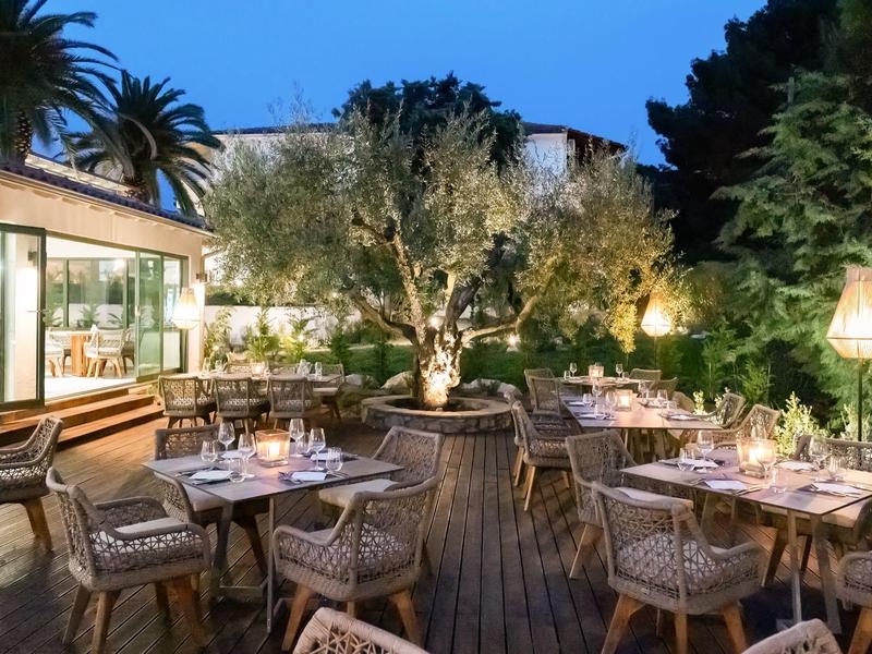 Restaurant extérieur chaleureux avec tables en bois, éclairage doux et verdure luxuriante au crépuscule.
