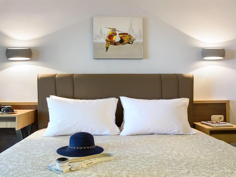 Chambre d'hôtel confortable avec lit double, lits superposés, tables de chevet, lampes murales et tableau au-dessus du lit.