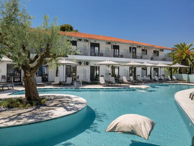 Piscine extérieure avec coussin devant un bâtiment d'hôtel de deux étages sous un ciel dégagé.