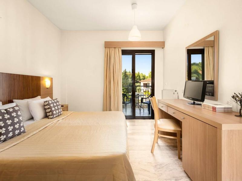 Habitación de hotel luminosa con cama doble, escritorio, silla y balcón con vista al área verde.