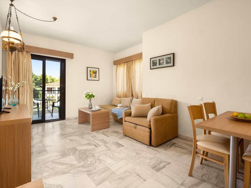 Una sala luminosa con sofá, mesa de comedor, TV y acceso a un balcón con vista a la vegetación.