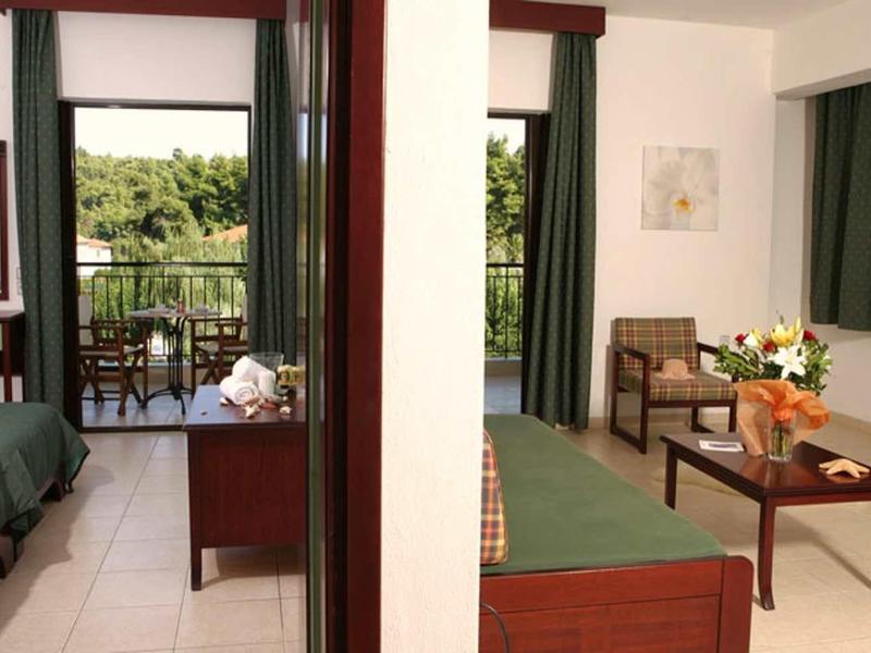 Habitación de hotel con cama doble, área de estar, escritorio y balcón con vista a paisaje verde.