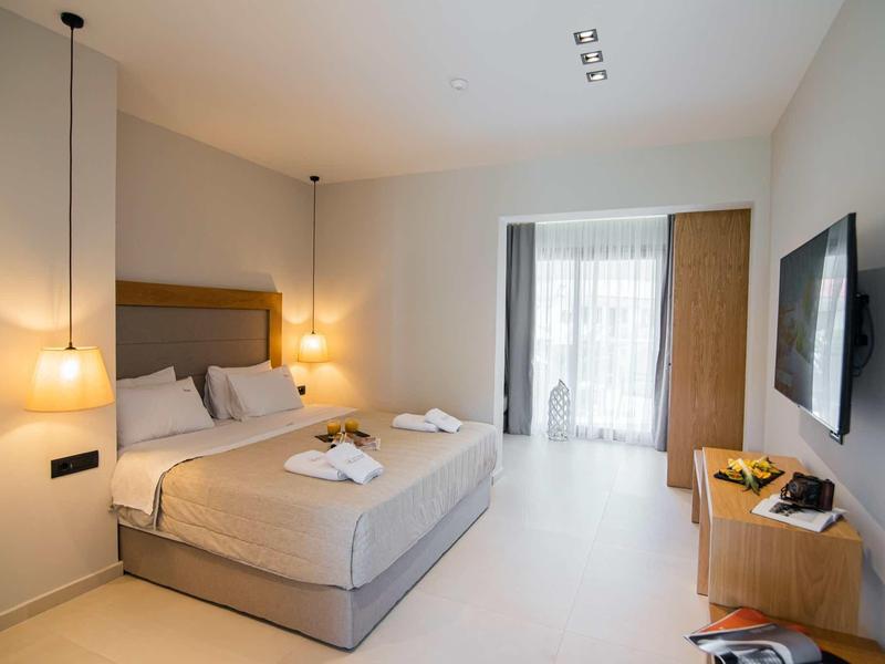 Habitación de hotel moderna con cama grande, luz cálida y ventana grande con cortinas.