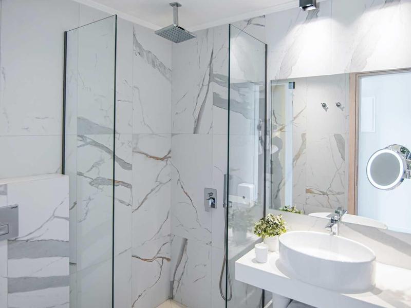 Baño moderno con ducha de vidrio, inodoro blanco y espejo grande con iluminación