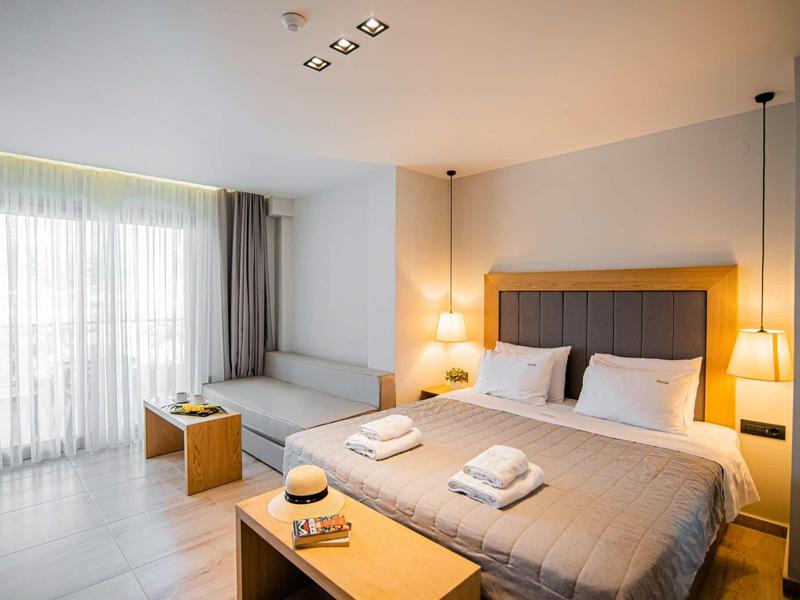 Habitación de hotel luminosa con cama grande, puerta ventana con cortinas e interior moderno.