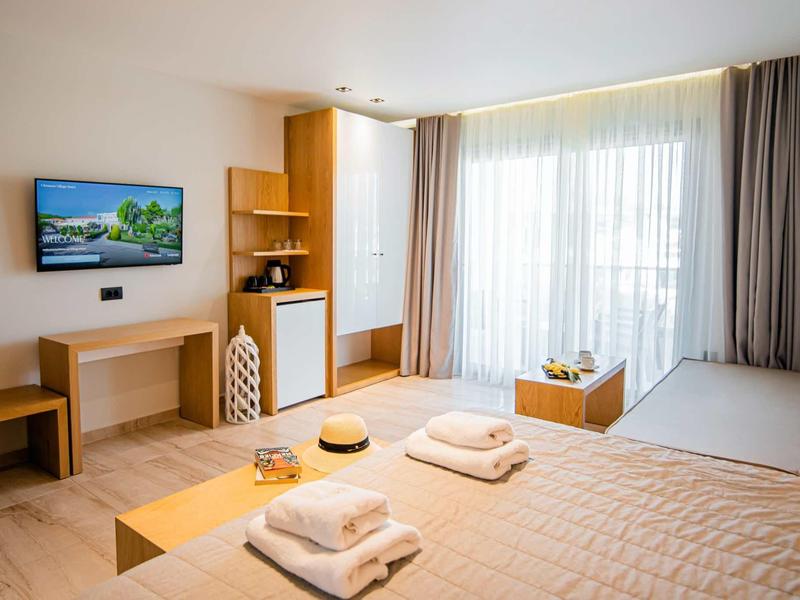 Habitación de hotel luminosa con cama doble, televisor en la pared y gran ventana con cortinas.