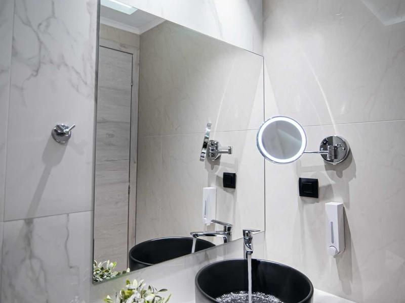 Área de baño moderna de hotel con lavabo negro, espejo e iluminación elegante.