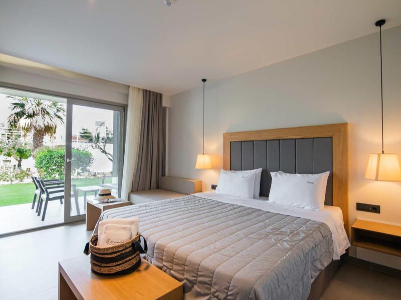 Habitación de hotel luminosa con cama doble y vista al jardín y terraza.