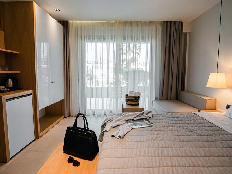 Habitación de hotel luminosa con cama doble, lámpara de noche y balcón con vista exterior.