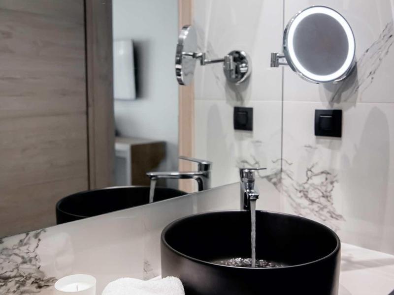 Lavabo negro moderno con espejo iluminado, toalla blanca y taza sobre encimera de mármol en baño de hotel.