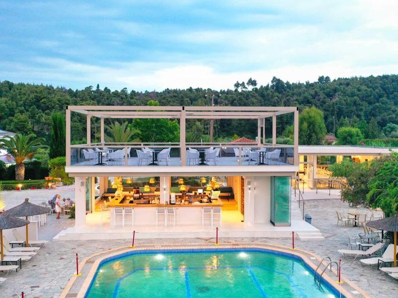 Piscina moderna de hotel con terraza, tumbonas y paisaje verde alrededor durante el día.