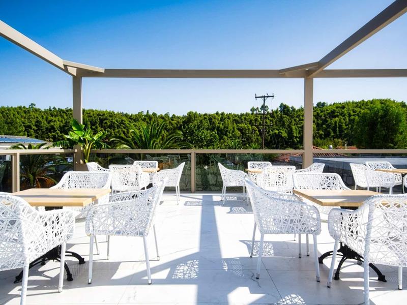 Área exterior moderna en una azotea con mesas y sillas blancas bajo un cielo azul.
