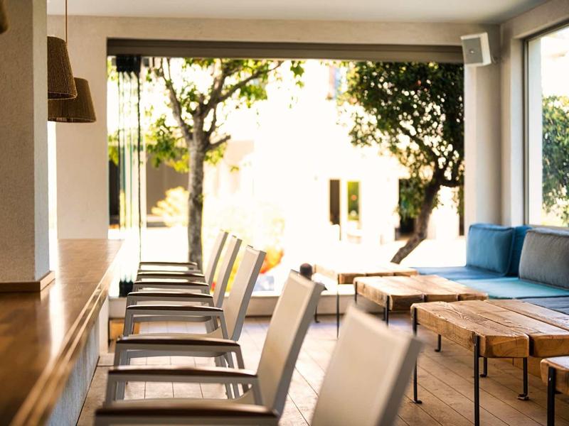 Área moderna de salón de hotel con sillas y sofás con luz natural y árboles afuera.