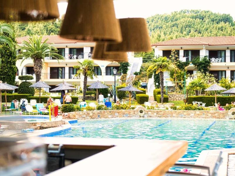 Área de piscina moderna con bar y asientos, rodeada de edificios y paisaje verde.