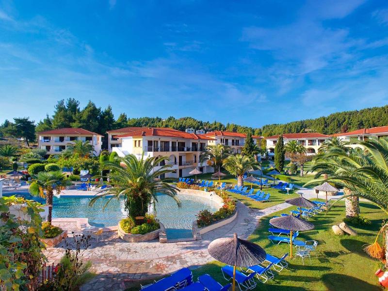 Vista de un complejo hotelero con piscina, palmeras y tumbonas bajo un cielo azul despejado
