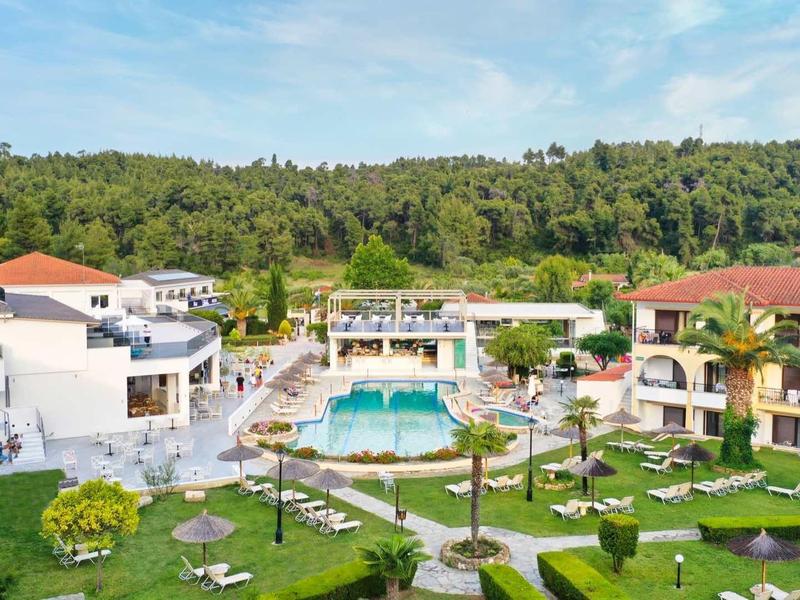 Complejo hotelero moderno con piscina y jardín cuidado frente a colina boscosa bajo el sol.