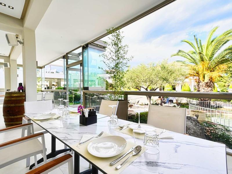 Terraza de restaurante con mesas preparadas y vistas a palmeras y un entorno soleado.