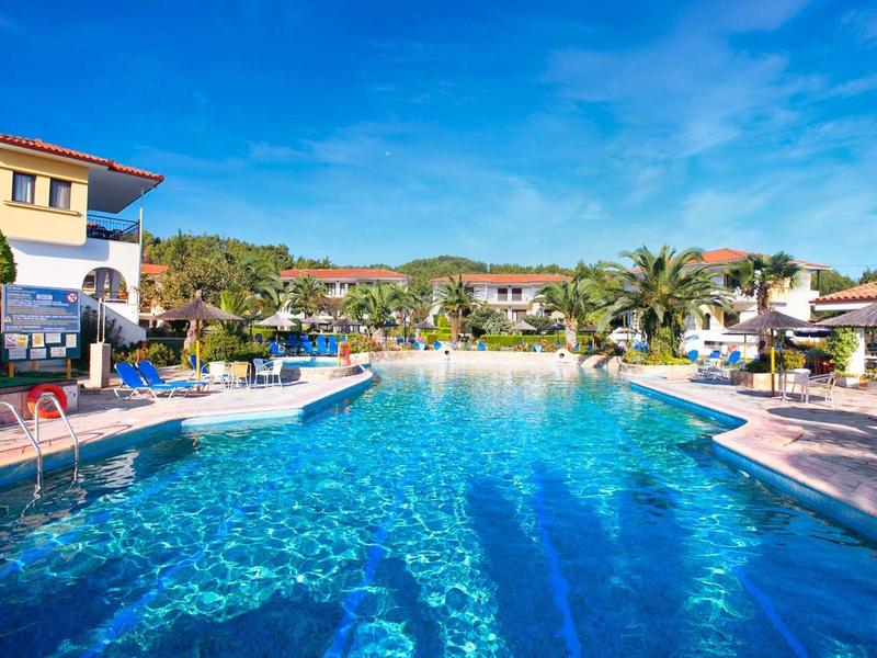 Gran piscina con agua clara rodeada de tumbonas y palmeras en un resort.